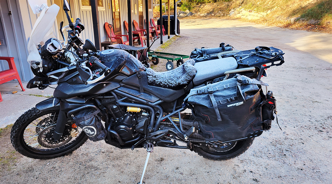 a motorcycle parked next to a motel on a autumn morning, its seat covered in frost.