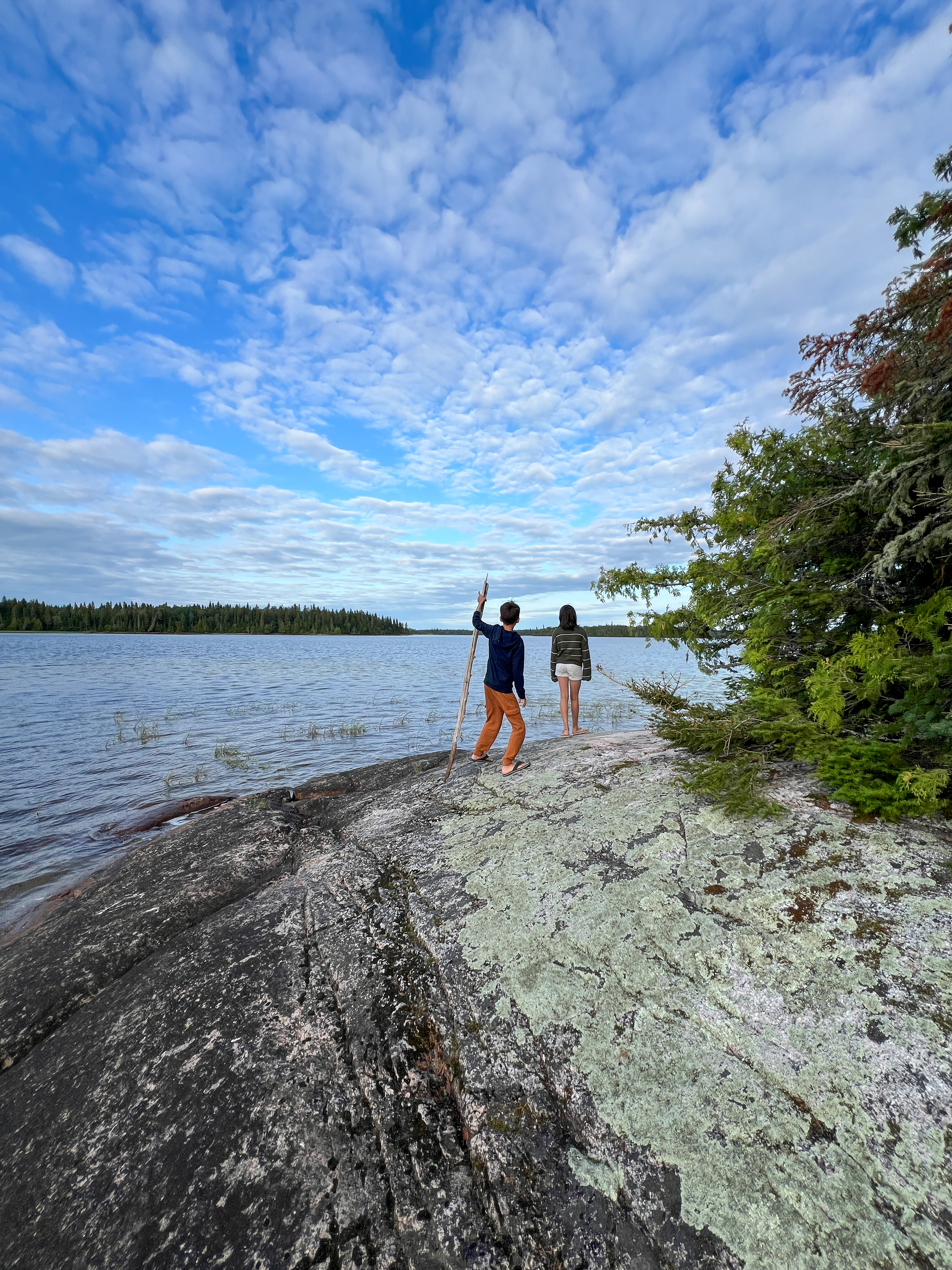 Two young children hiking on a rock near a lake