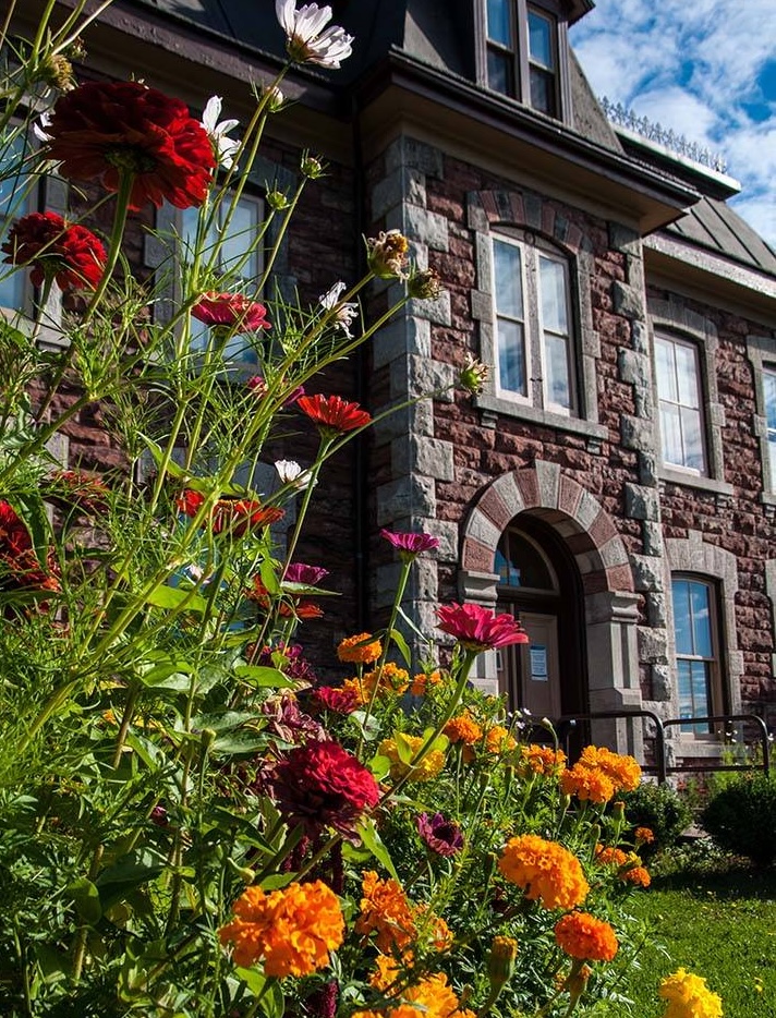 one of the opulent stone historical buildings a the Sault Ste. Marie Canal National Historic Site, with a lush green grass and large red and orange flowers in the foreground.