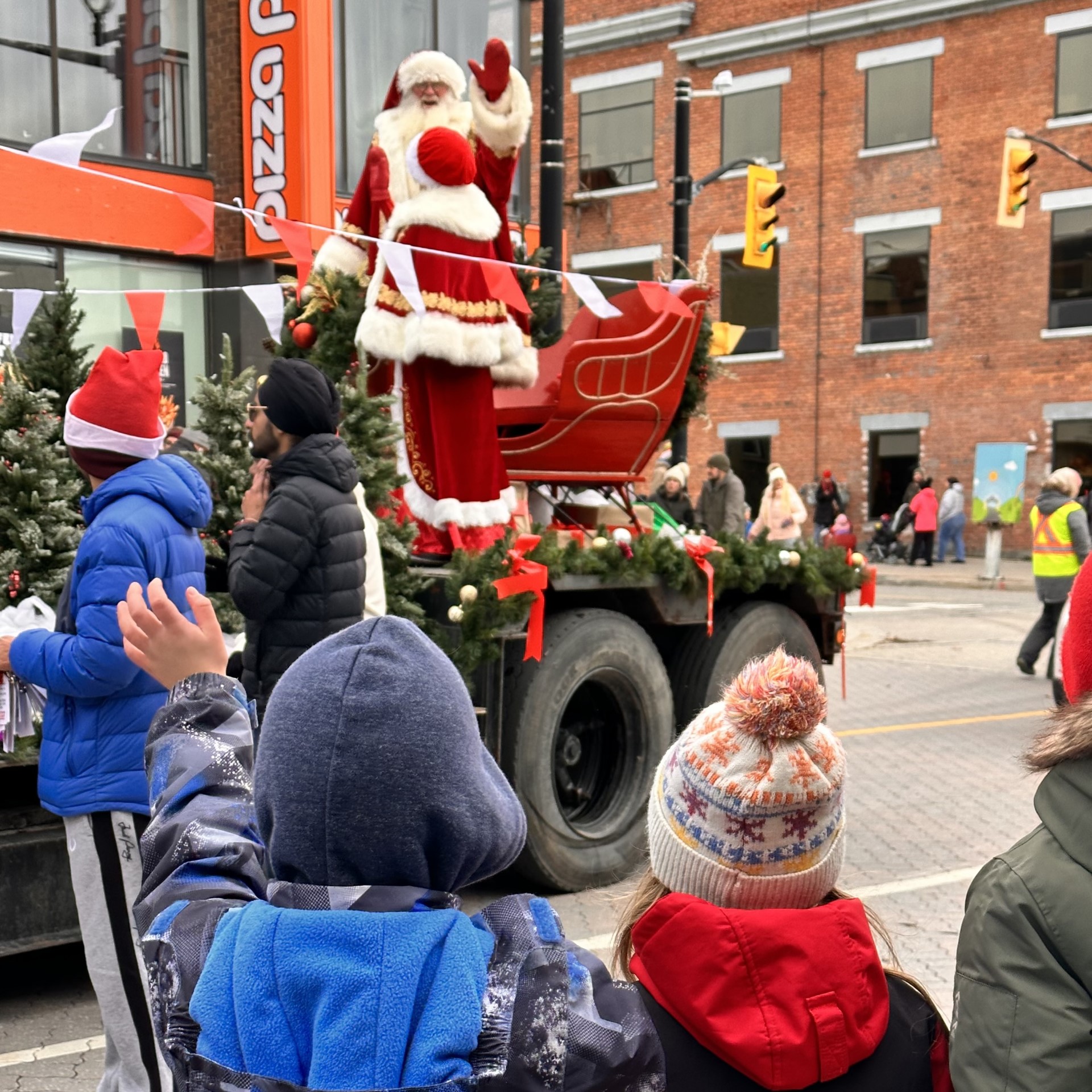 a Santa Clause waves from the back of a parade float while children watching wave back