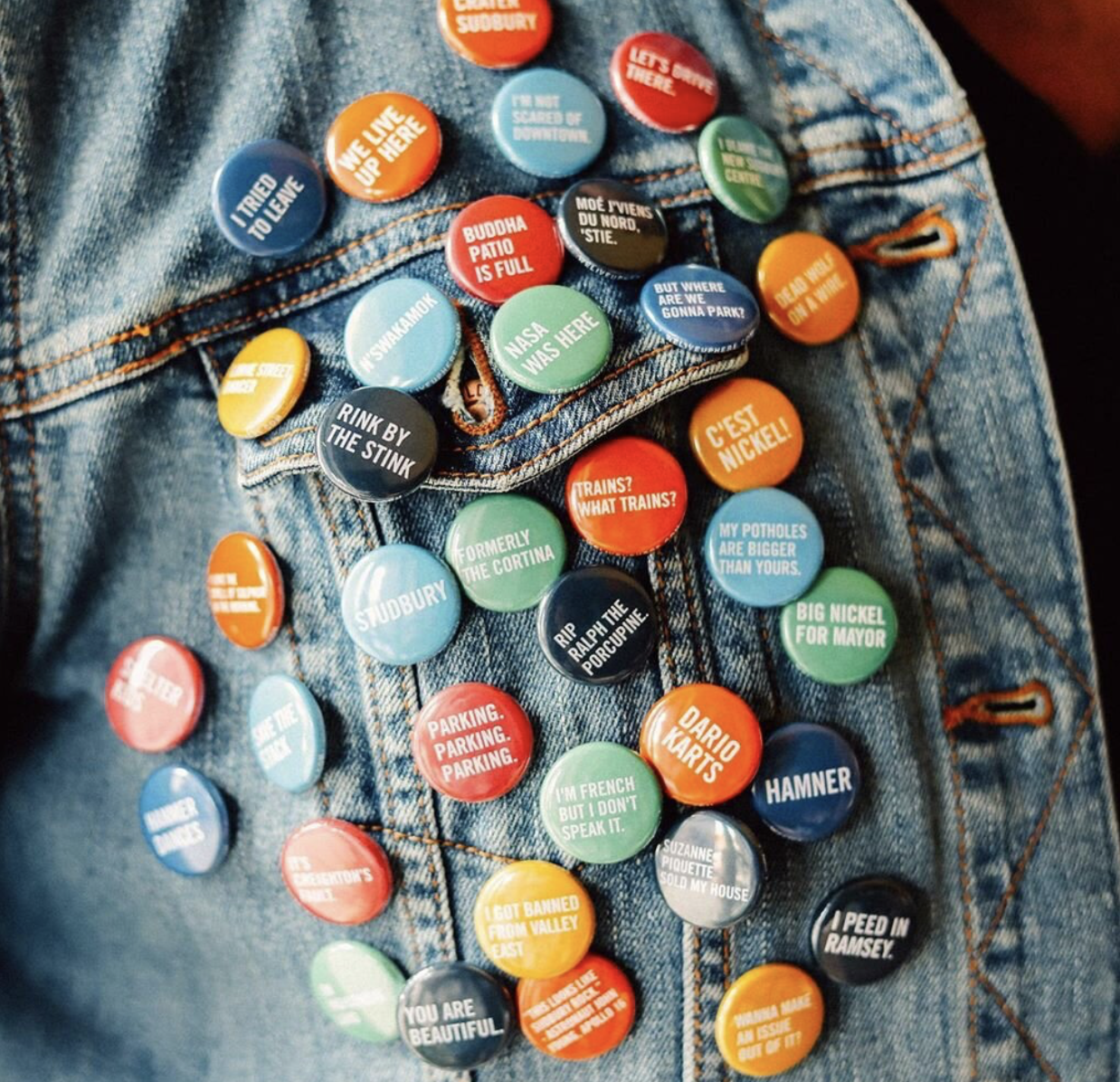 a series of colourful buttons featuring sayings in white text, pinned to a denim jacket