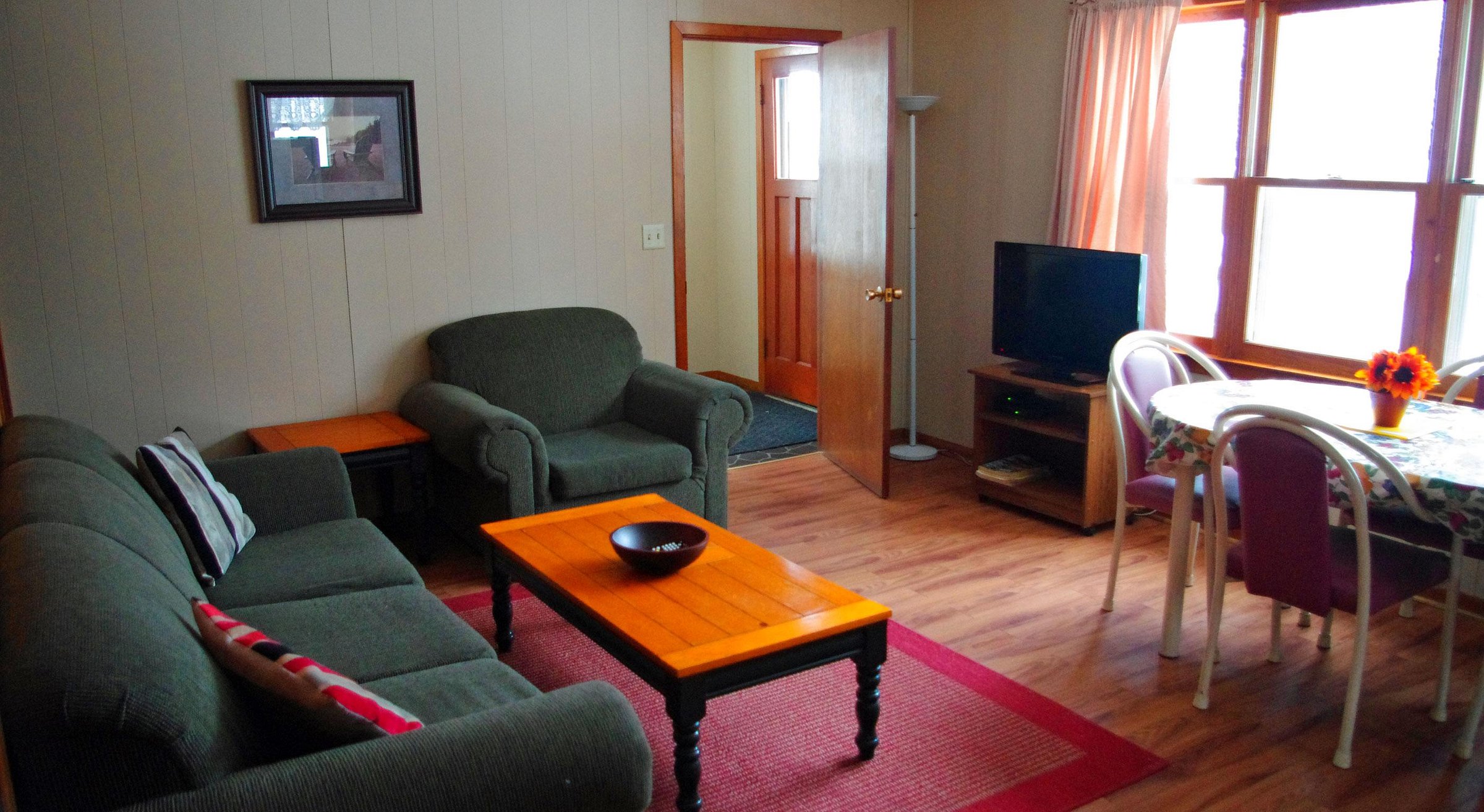 a tidy cottage sitting area with couch, armchair, coffee table and bright windows.