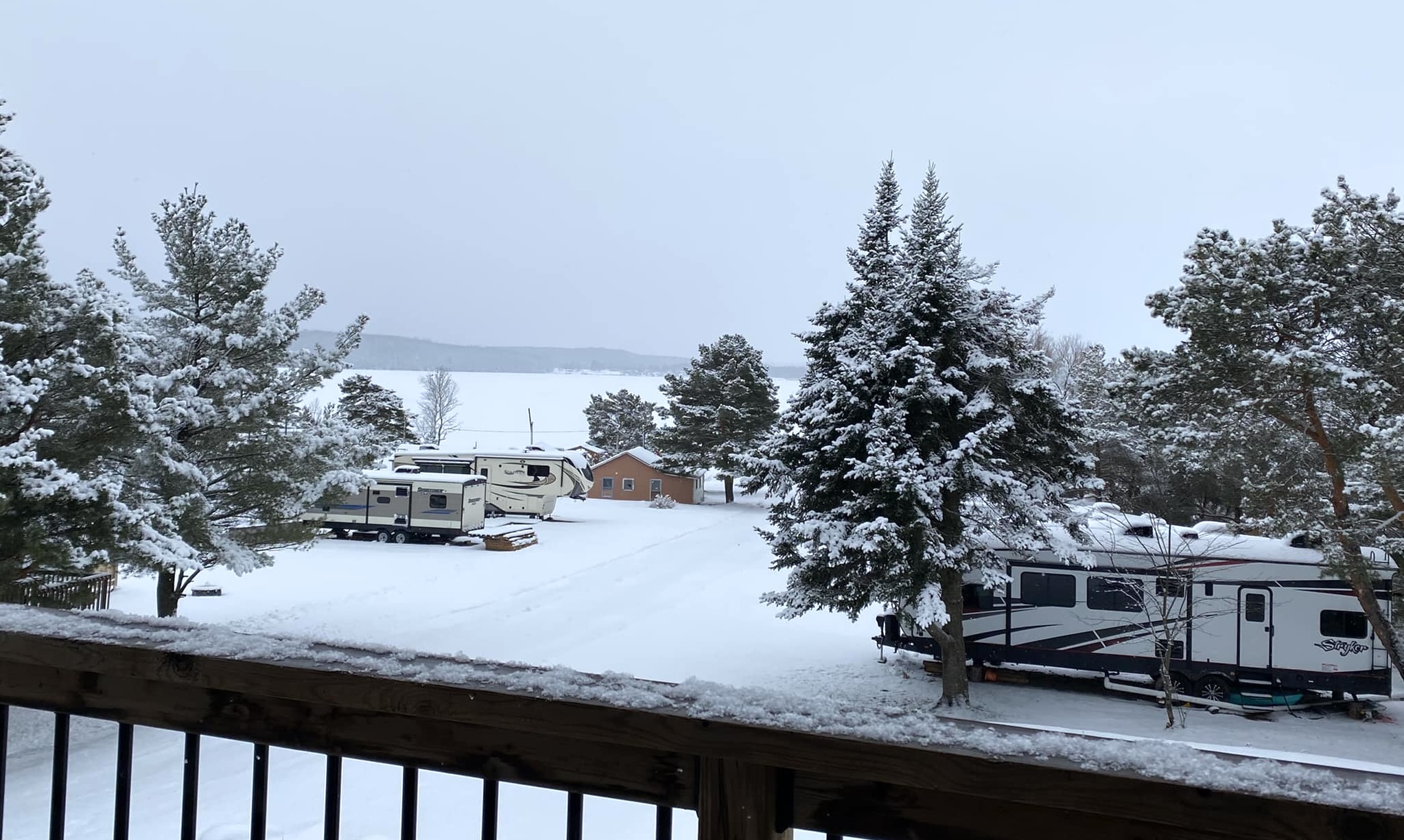 peaceful, snow covered RVs and trees on the edge of a large snow covered lake under a grey cloudy sky.