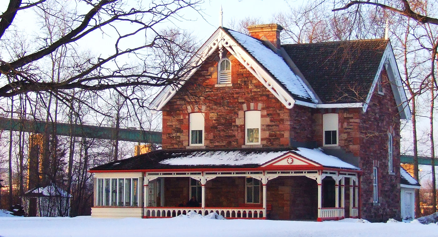 Winter at the Superintendant's Residence at the Sault Ste. Marie Canal National Historic Site; a large stone Gothic-Revival style house with an opulent covered porch.
