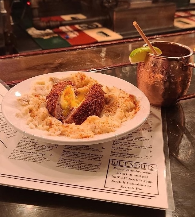 A Scotch Egg plated with mashed potatoes, sitting on top of a menu at the Whiskey Barrel.