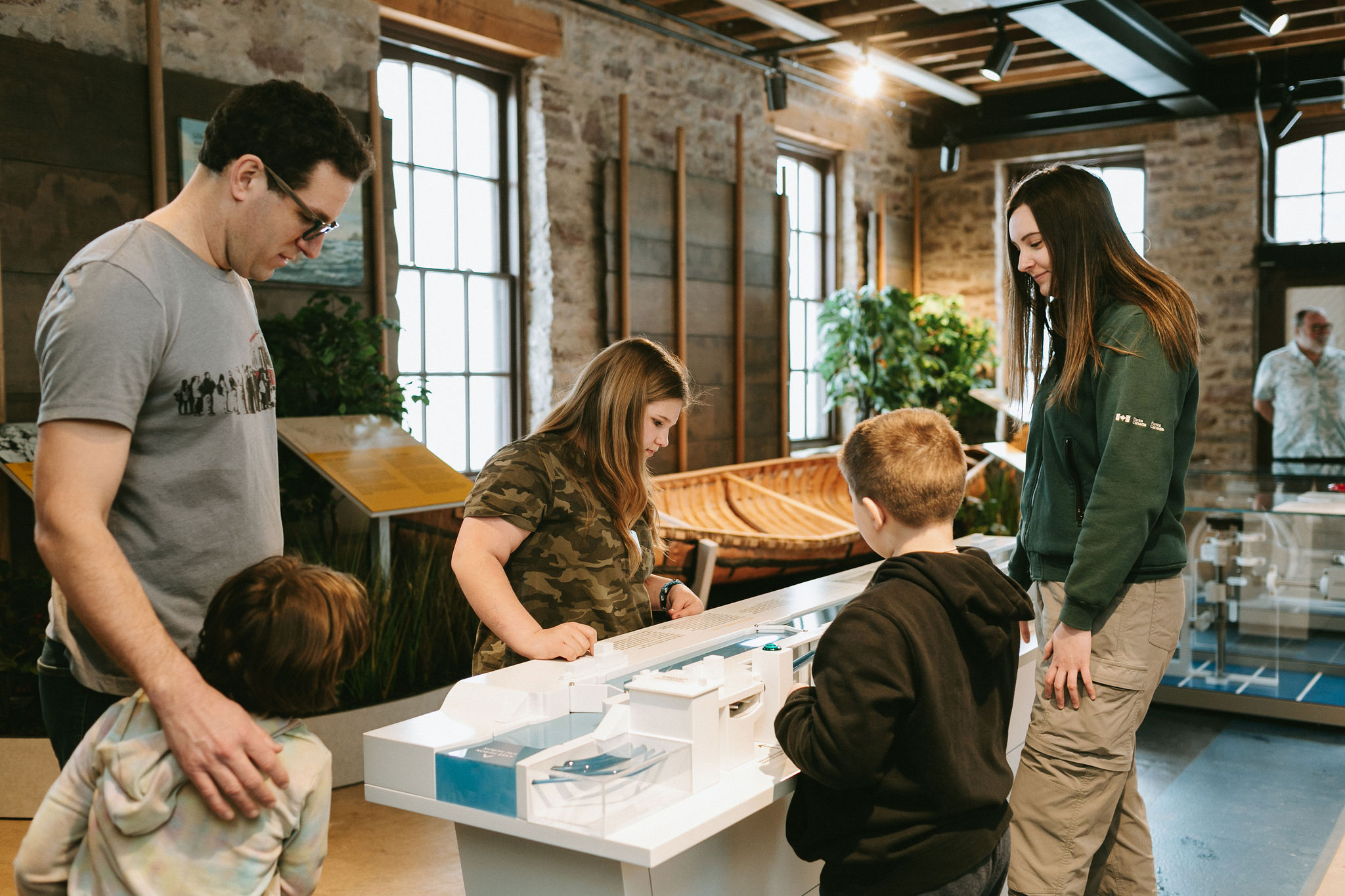 A family looks at a display in the Sault Ste. Marie National Historical Site visitors' centre, while a smiling park employee talks to them.