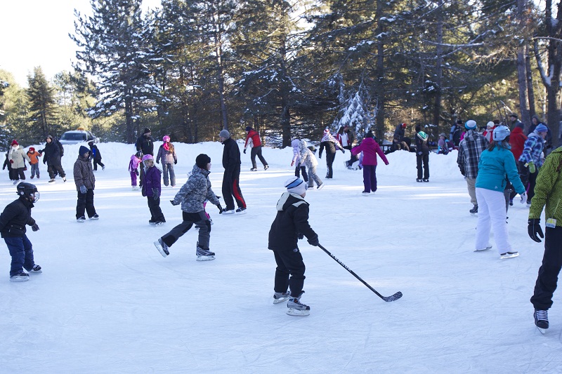 children skate and play hockey on a frozen pond surrounded in forest at Algonquin Provincial Park.