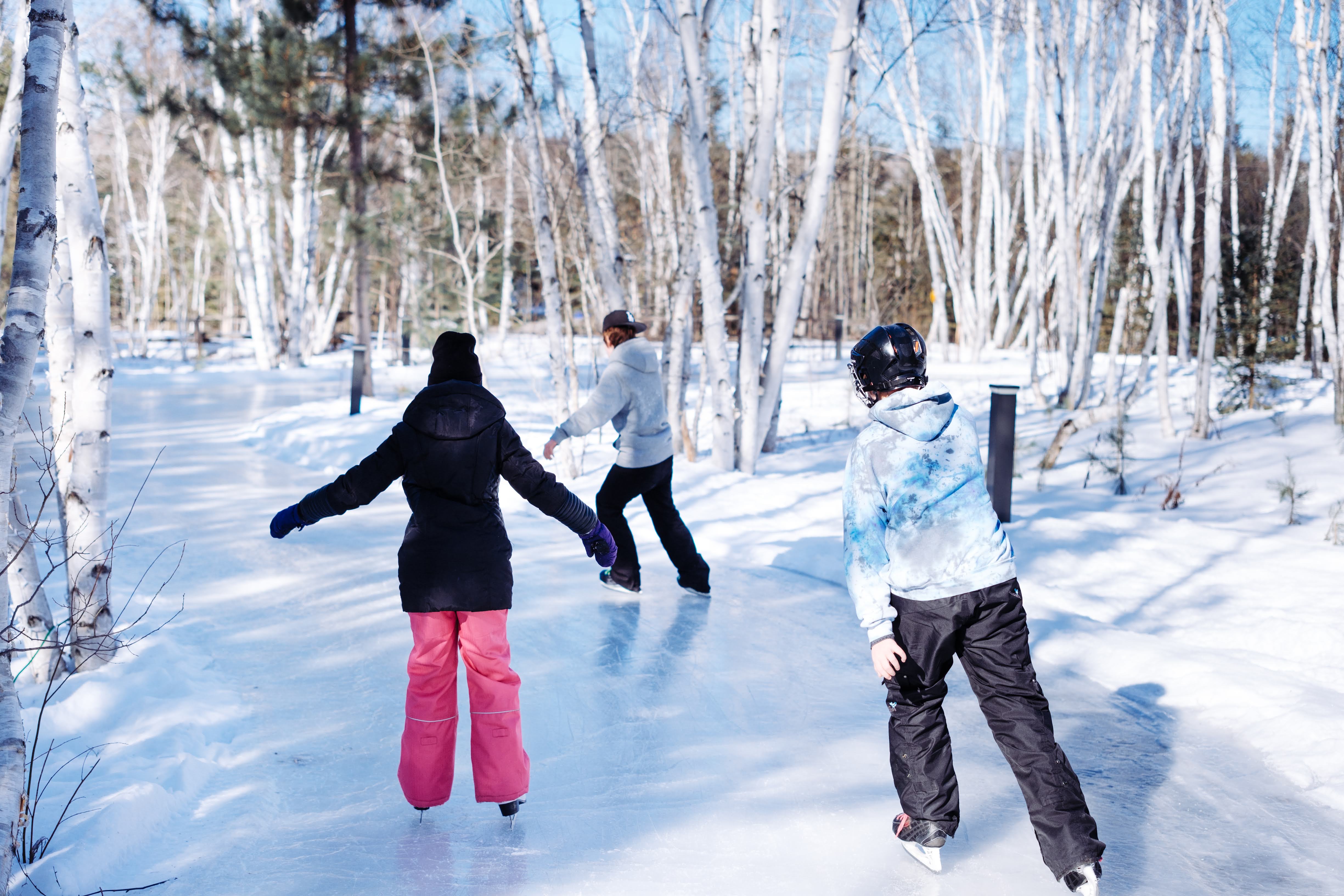 3 children skate down a skating trail through a winter forest on a sunny day.