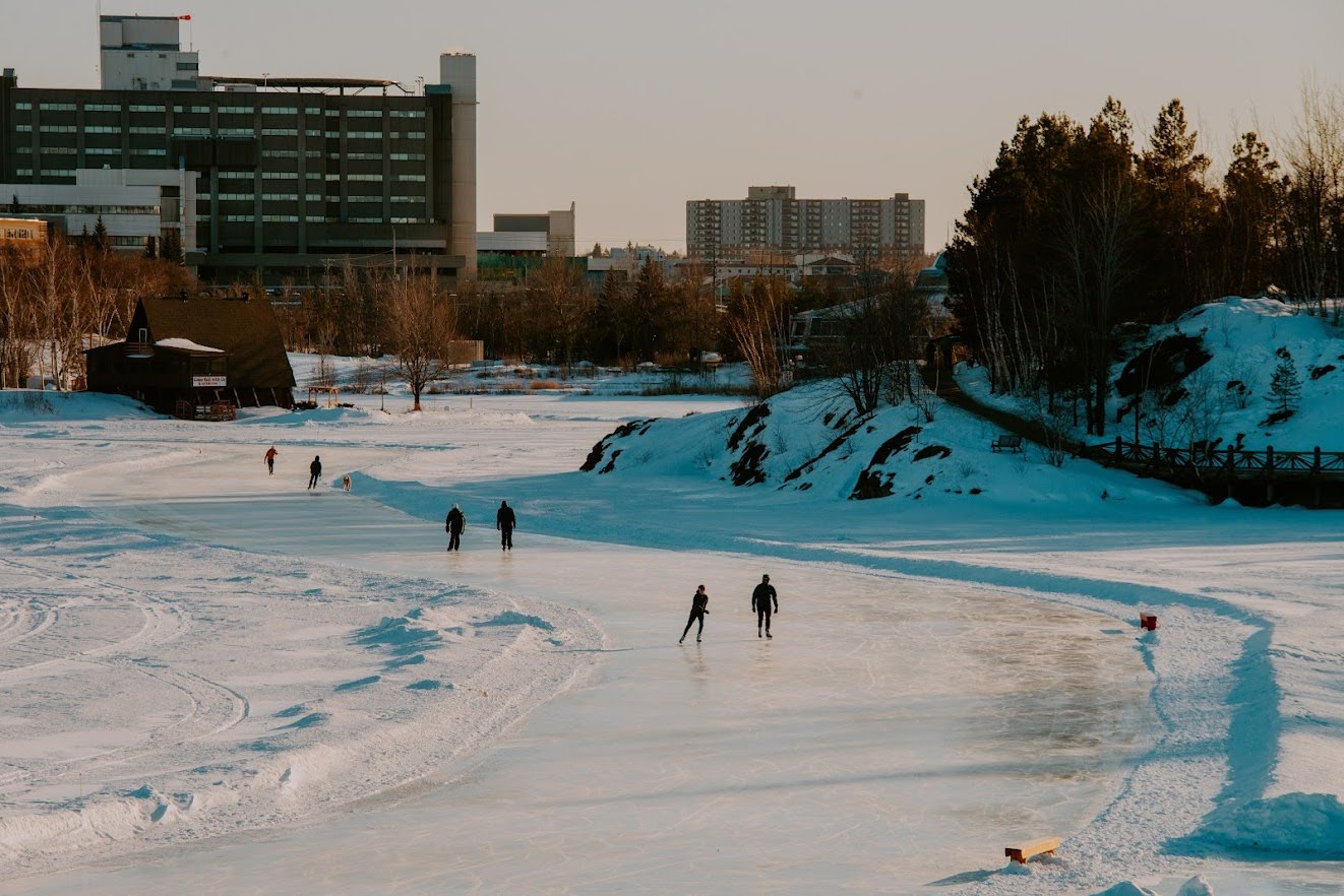 couples skate along Ramsey Lake Skate Path on a winter day, with the Sudbury cityscape in the backround.