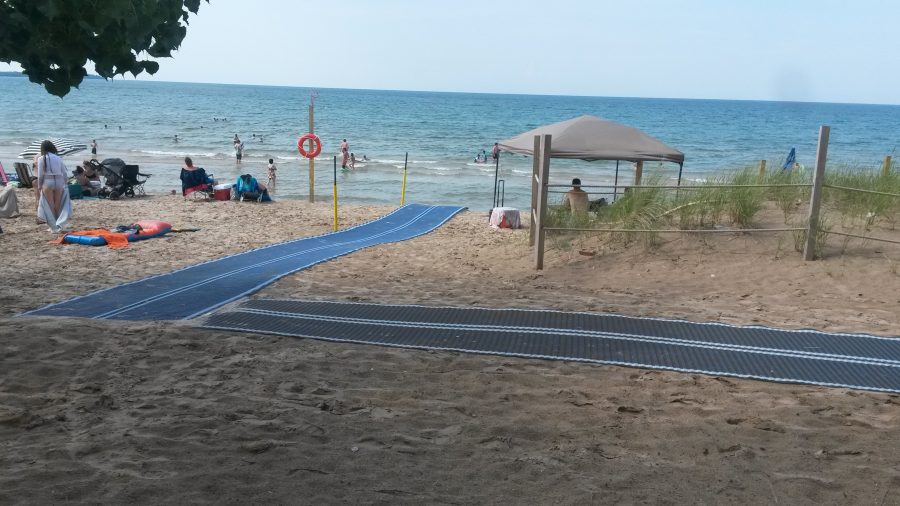 long rubber mats form an accessible path over a sandy beach to the shoreline of a large lake.