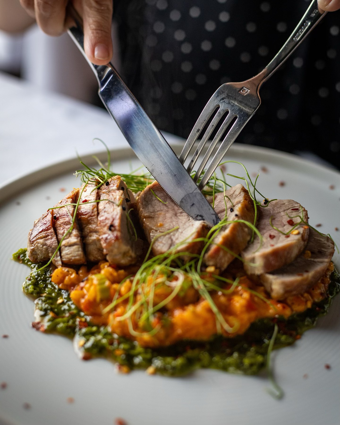 A stylishly plated dish of prime rib with sauces, and a person cutting into it with fork and knife.