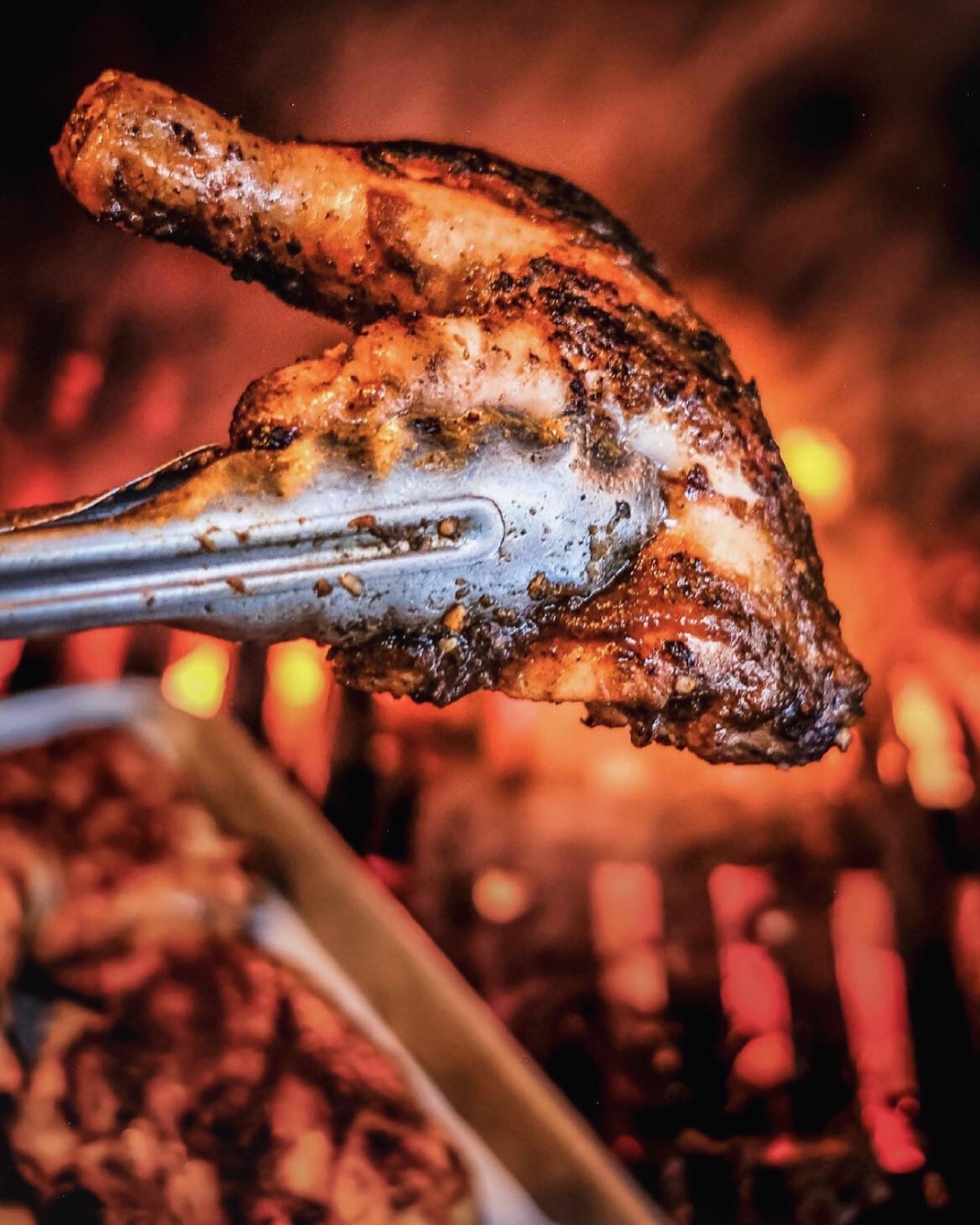 a piece of jerk chicken being held up by tongs over a flaming grill.