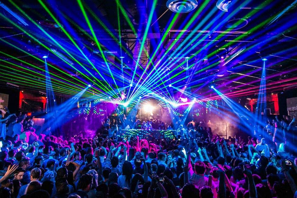 a night club crowd dances while mulitcoloured lasers criss cross above their heads.