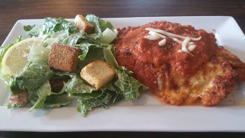 A chicken breast and caesar salad on a white plate.