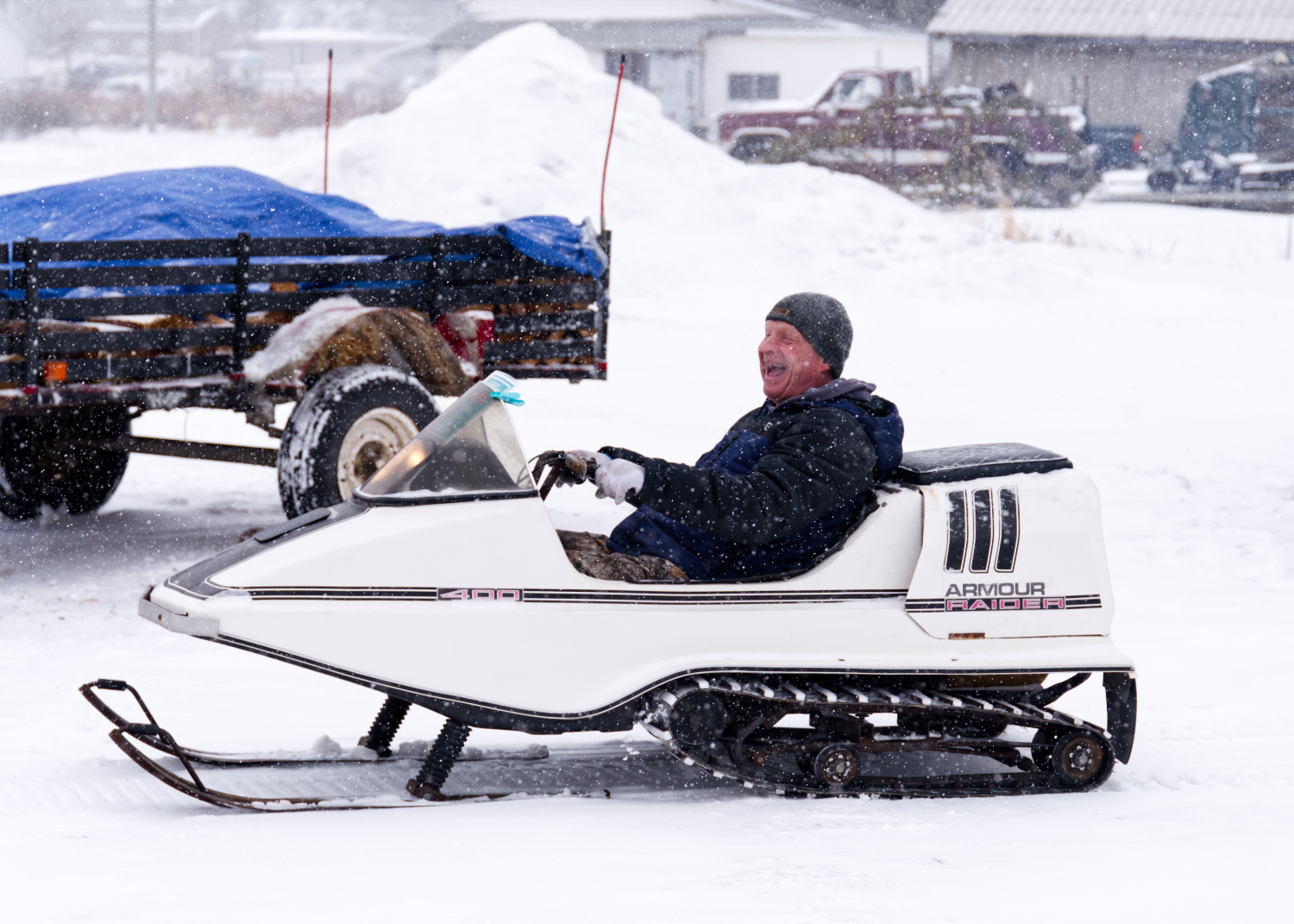 A man smiles as he rides his vintage 1972 Raider snowmobile at Big Winter Festiglace on a snowy day.