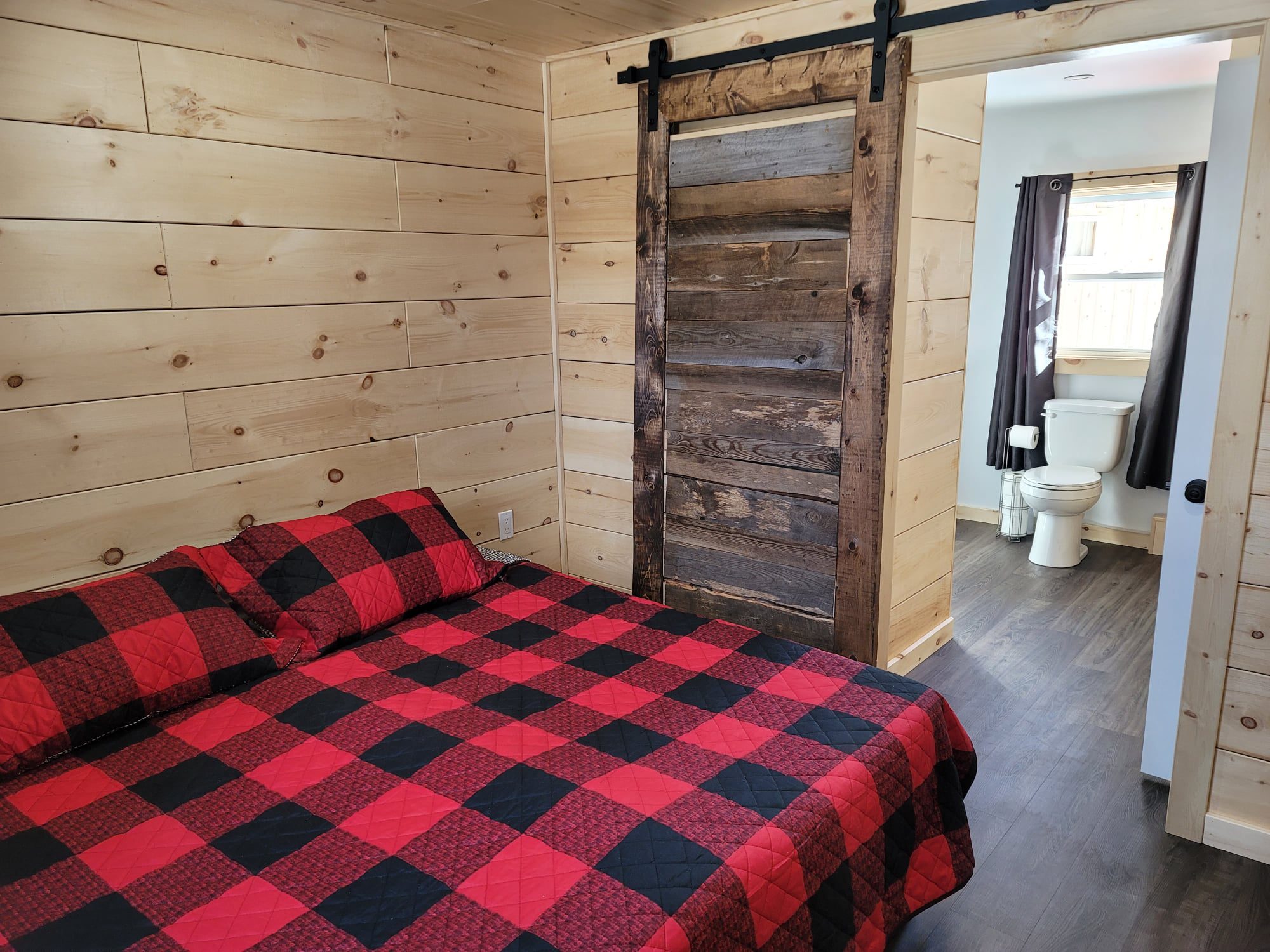 A bedroom featuring a bed with a black and red checkered bedspread. The walls are made of pine.