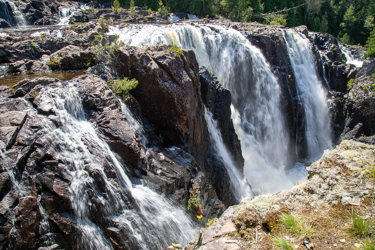 Aubrey Falls; a steep rushing waterfall over rock cliffs surrounded by green boreal forest.