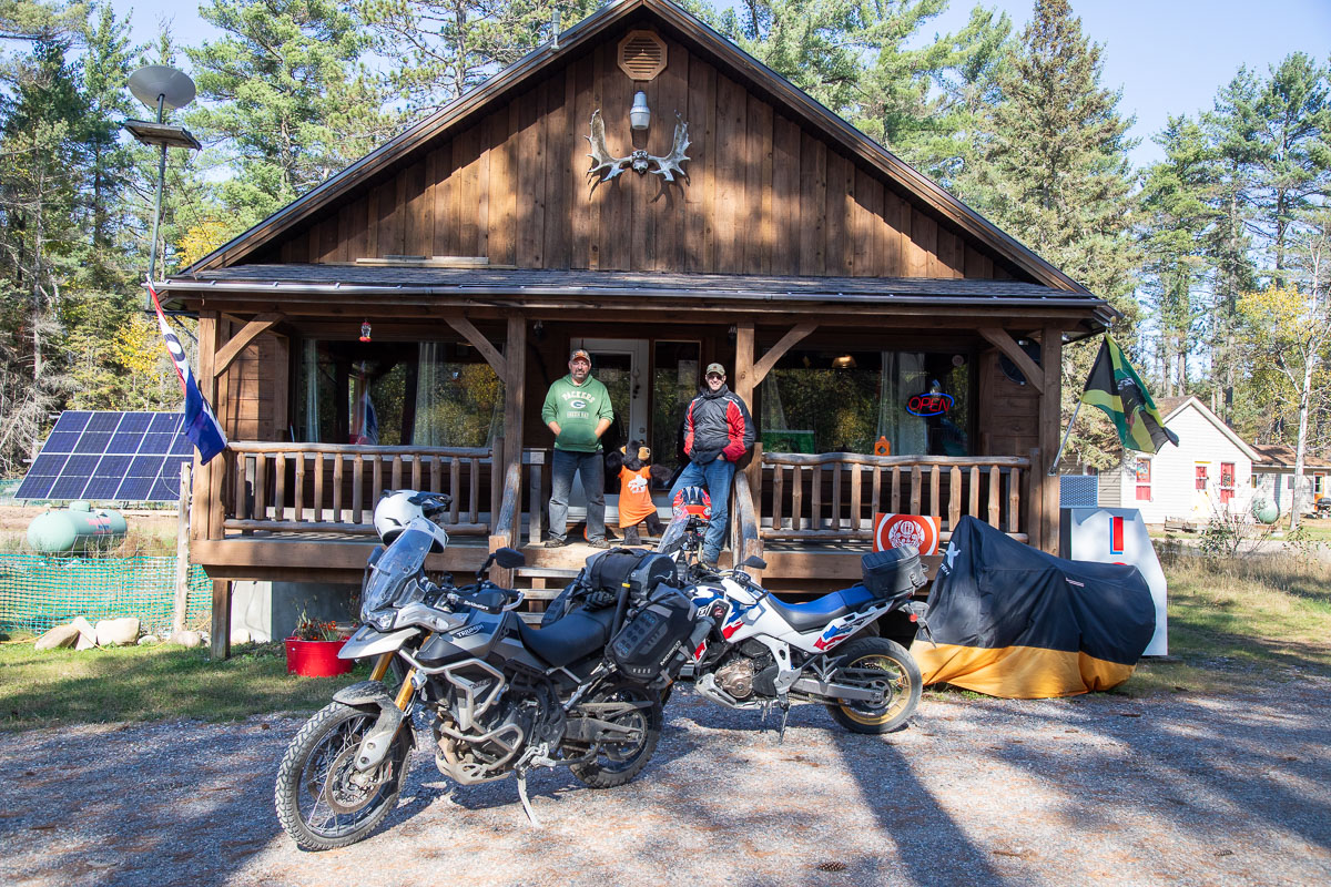 2 motorcyclists standing on the front porch of a wooden cabin that is Black Creek Outfitters.