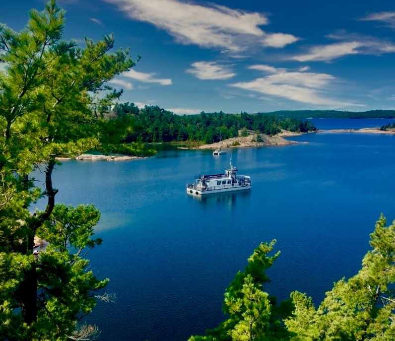 A cruise boat floats along the North Channel; the water and sky are a vivid blue and the forested banks are a lush green.