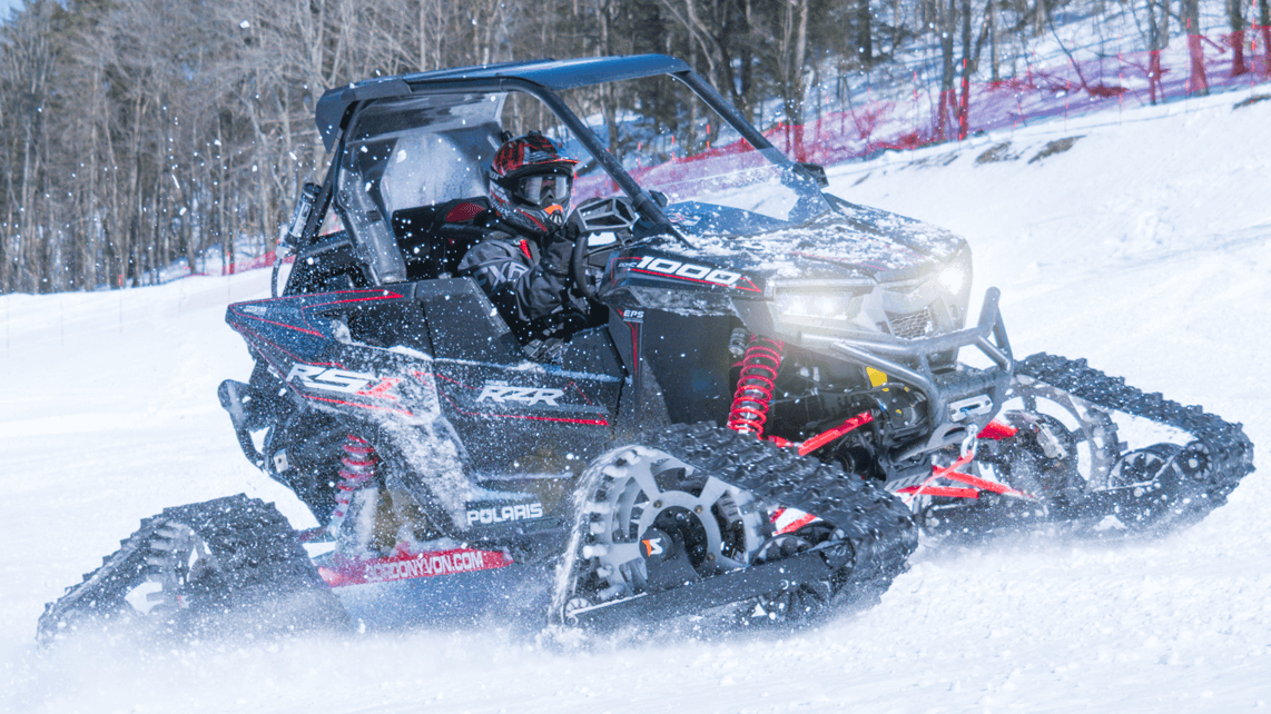 an ATV on tracks rolls up a hill in blowing snow.