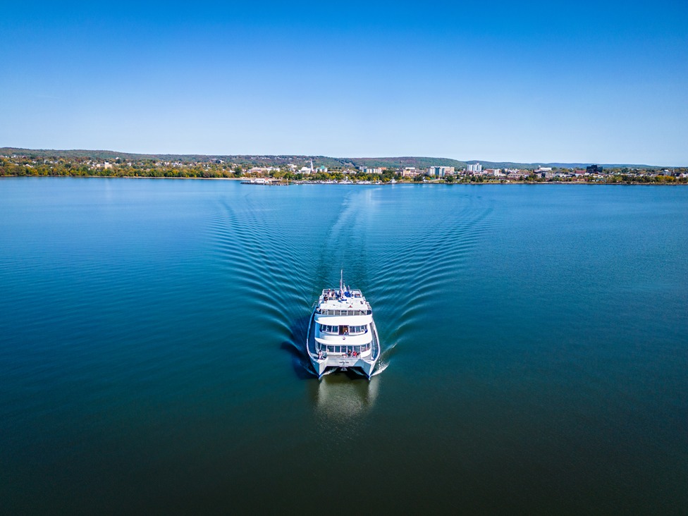 The Chief Commanda II ship glides along the glassy blue lake under a clear blue sky, the North Bay skyline on the horizon.