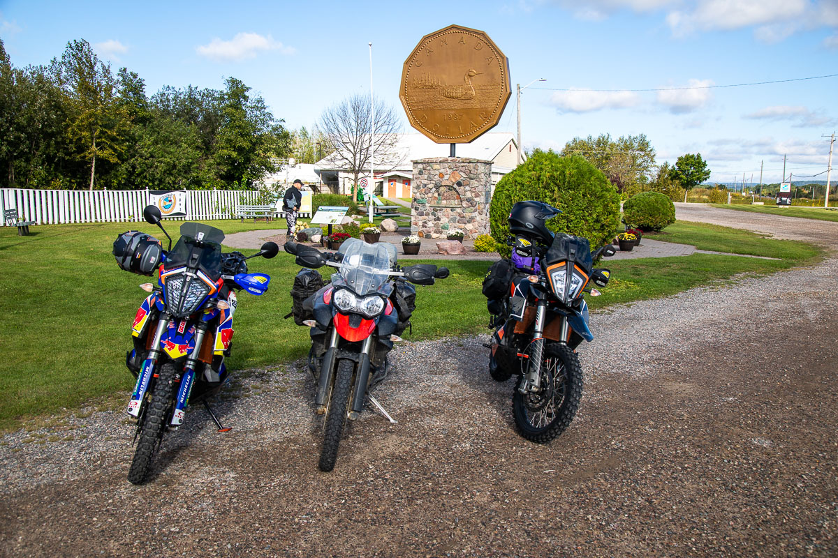 3 motorcycles parked in front of a monument of a giant Canadian one-dollar coin on a summer day. 