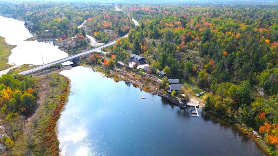 Great Escape Cabins; Glassy river water surrounded by vibrantly changing autumn forest with a row of cabins and docks along the water.