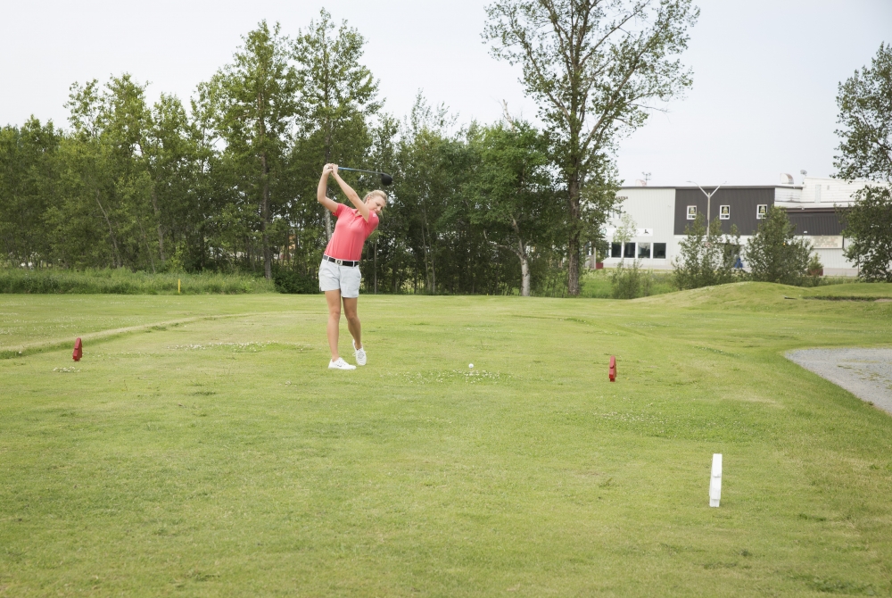 a woman golfing on a lush green course in the summer.