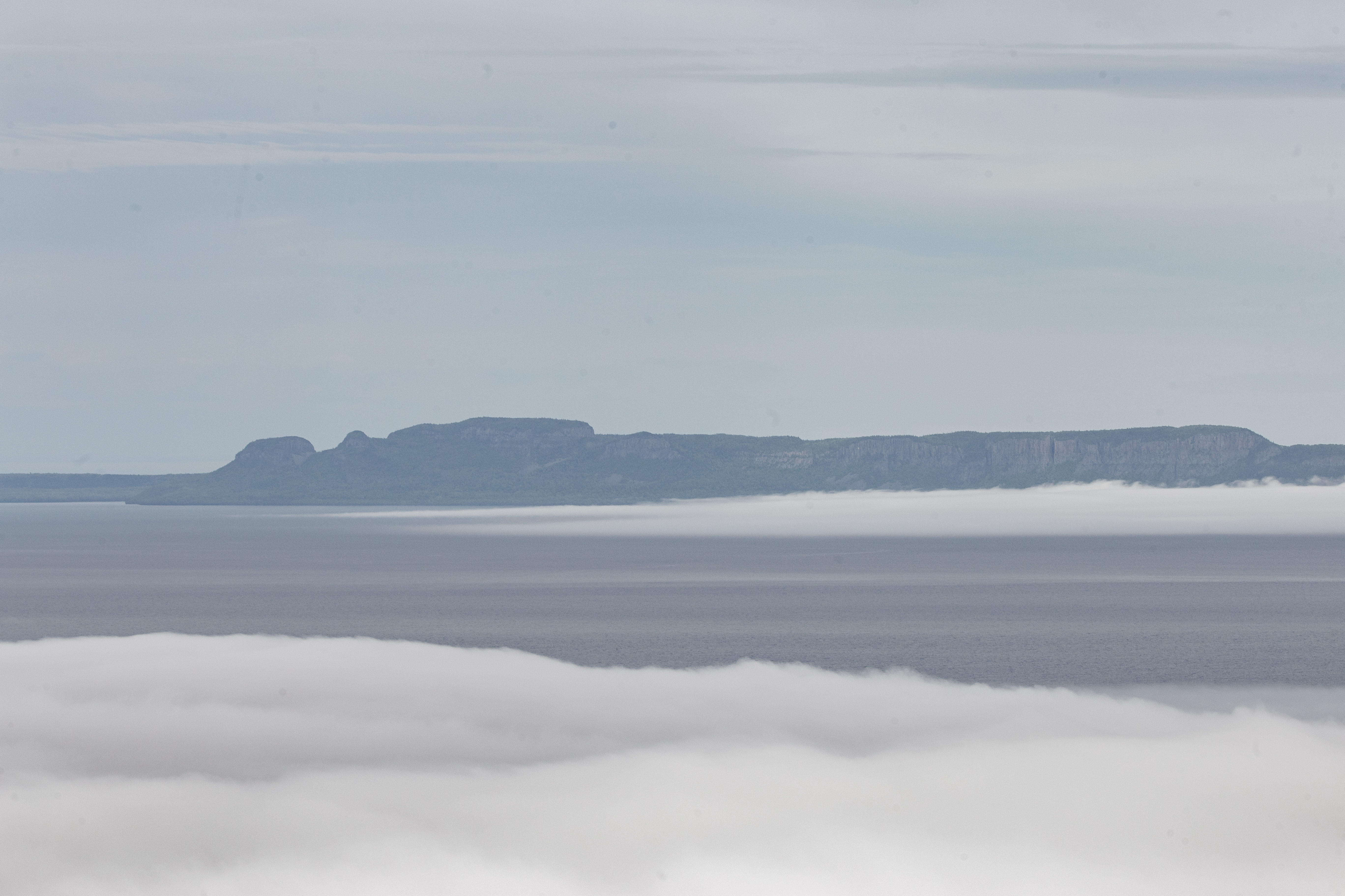 Sleeping Giant in the winter; a hazy rock ridge on the horizon, grey lake water, ice and snow in the foreground.