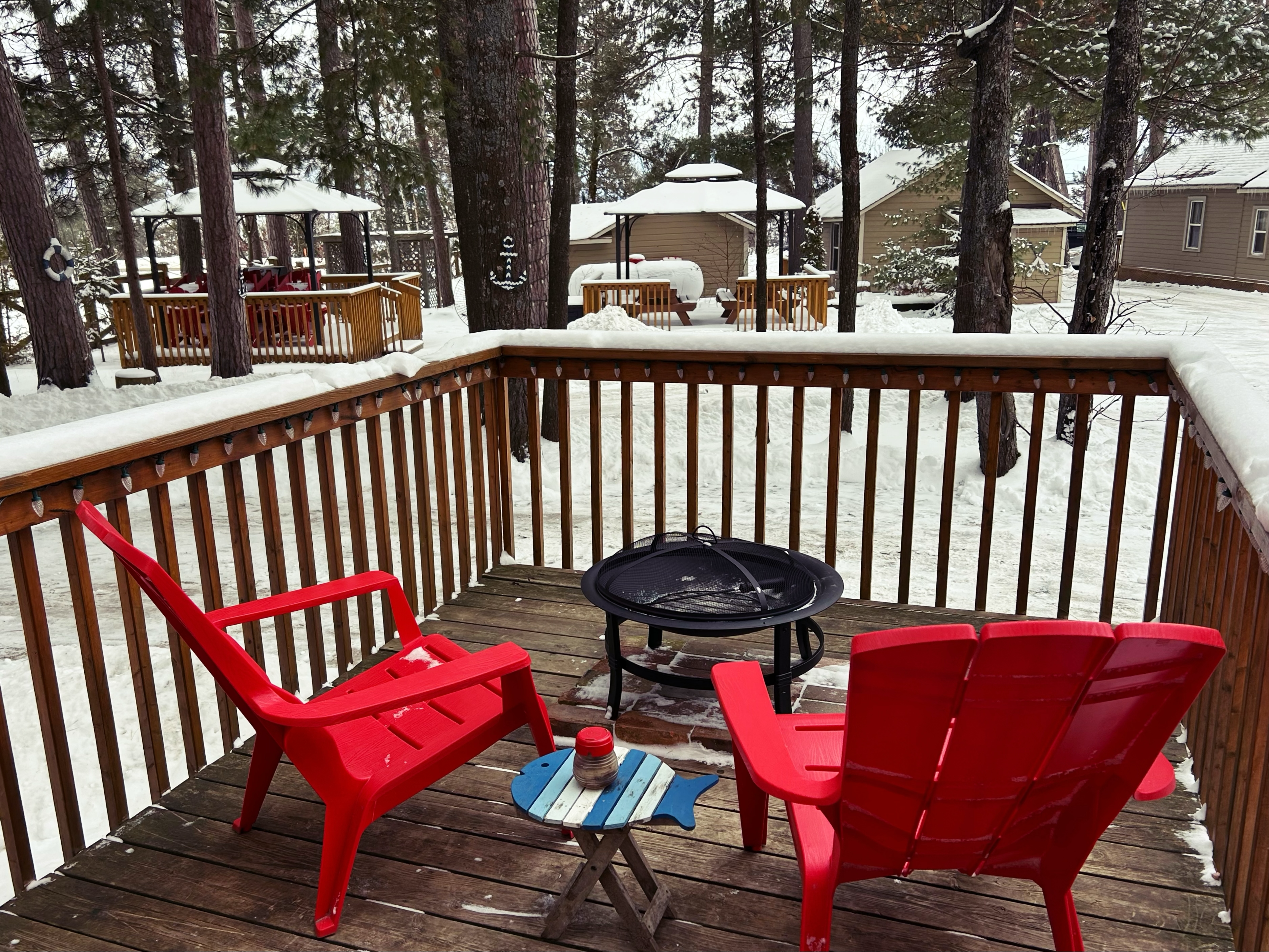 A deck with two red muskoka chairs in winter.