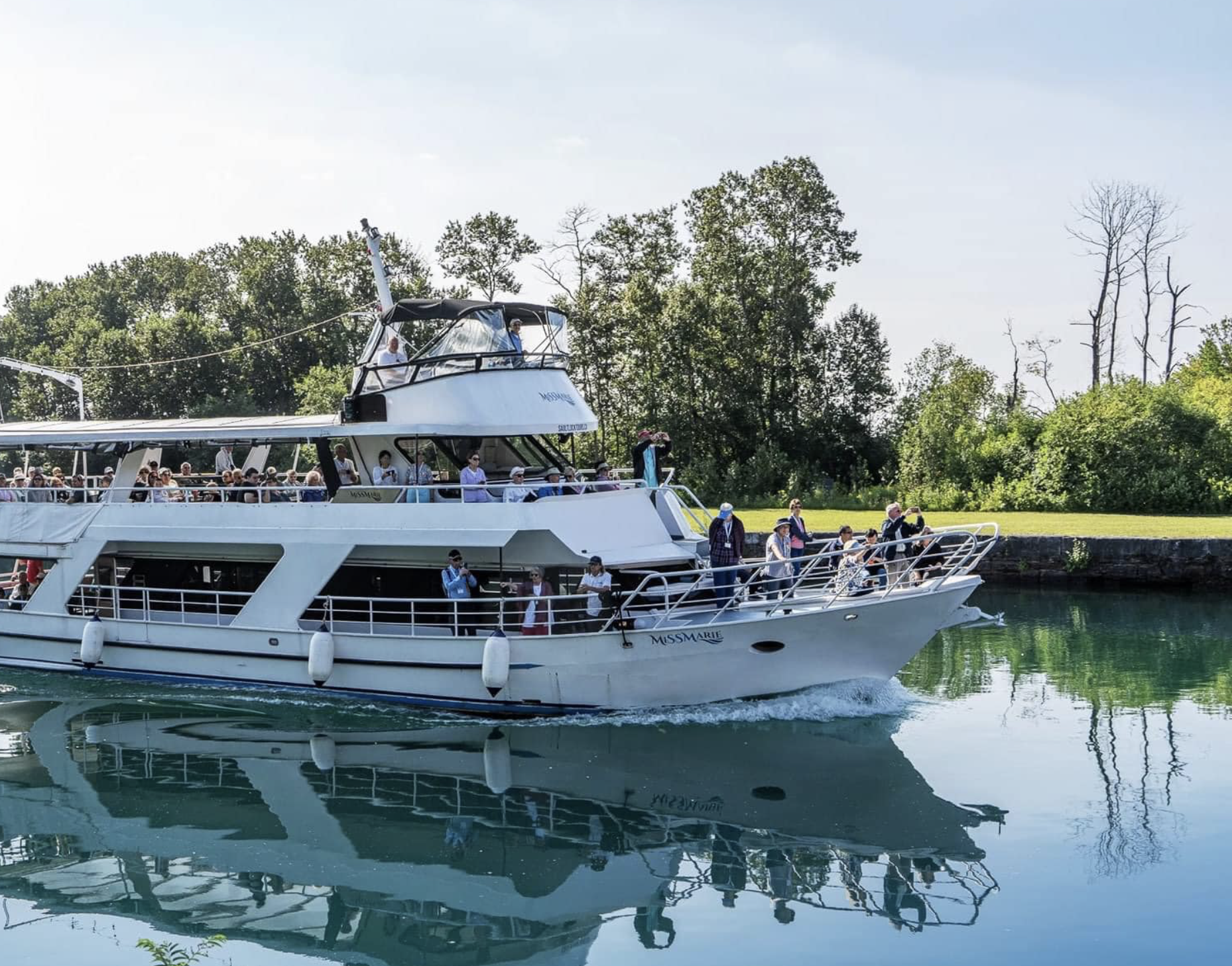 The Miss Marie passenger ship cruises up the light blue water of Sault Ste. Marie Locks on a sunny summer day.