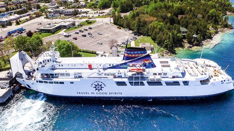 The MS Chi Cheemaun at port; a huge cruise ferry sitting in a tourquoise bay surrounded by green forest.