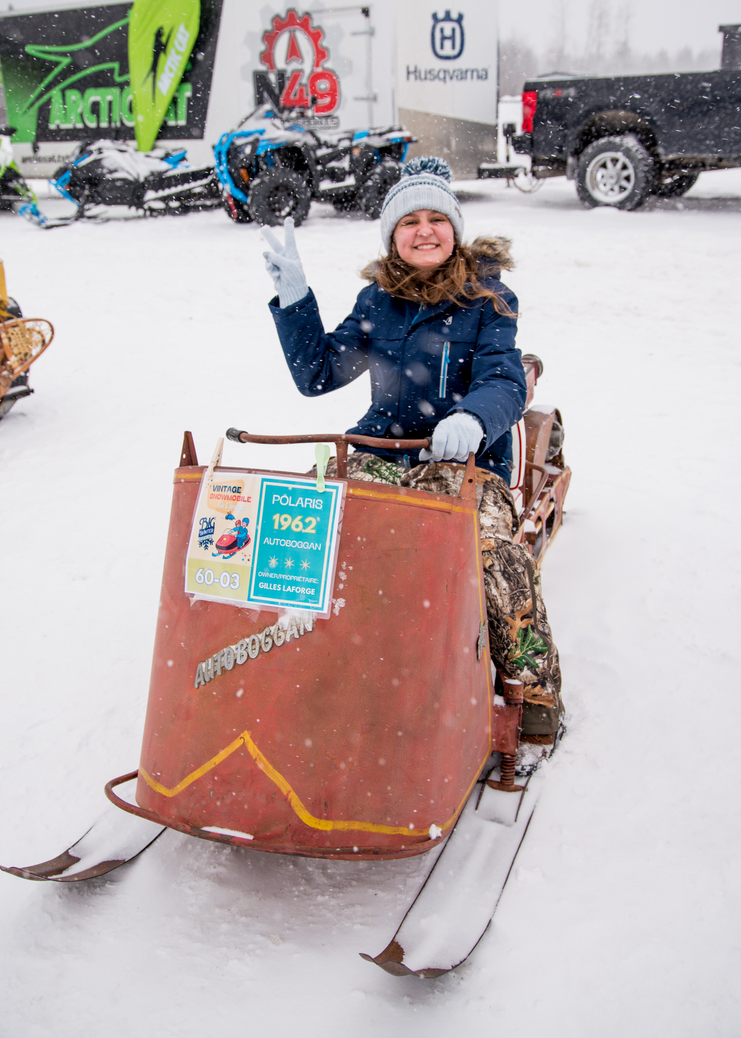 a smiling girl sits on a vintage Polaris 1962 Autoboggan at the Big Winter Festiglace on a snowy day.