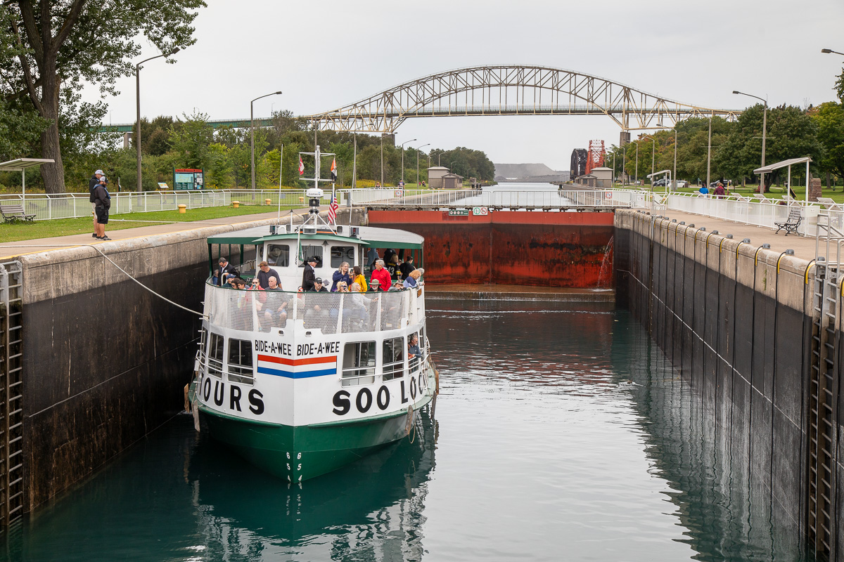 A boat with "Soo Lock Tours" painted on the hull floats in the Sault Ste Marie lock on a summer day. 