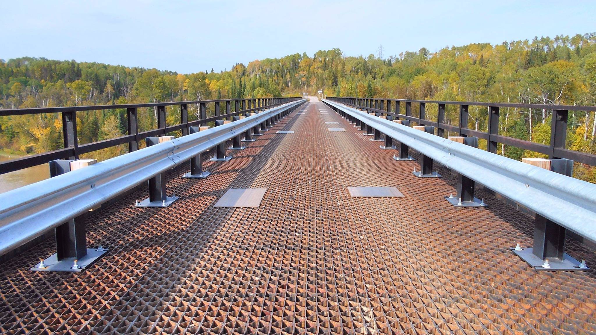 An iron trestle bridge stretching off to a thick green forest and clear blue sky in the distance.