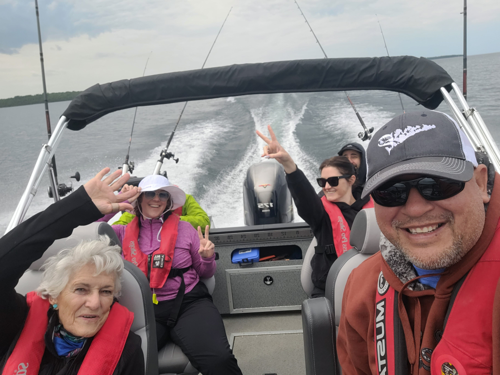 passengers wearing life jackets cheer with their arms raised while speeding down the lake in a Wass tour boat. The driver is smiling.