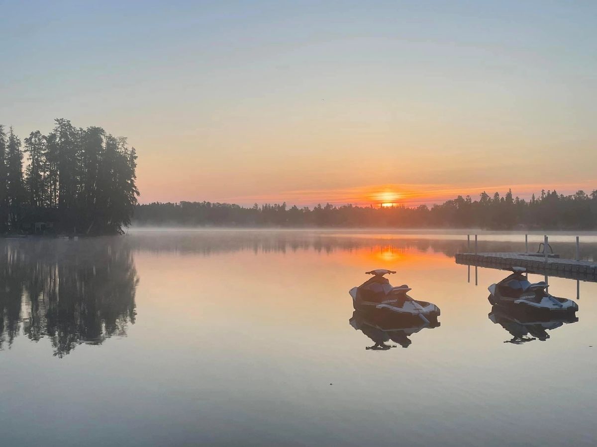 two PWCs parked next to a beach on a glassy calm lake under an orange sunset.