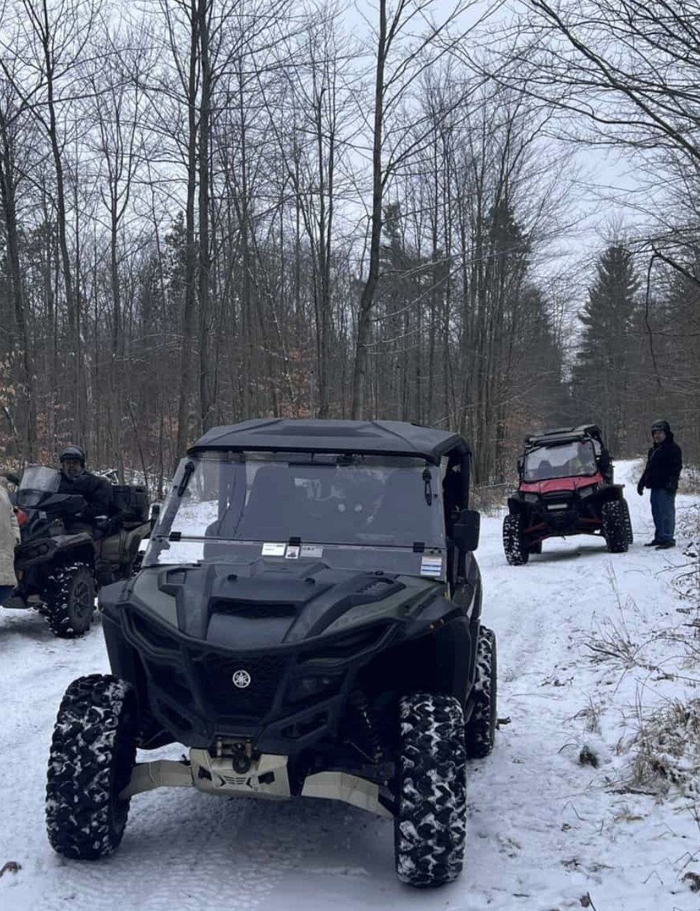 ATVs drive down a snowy forest trail.