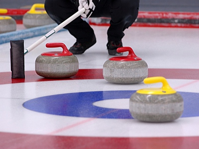 3 curling rocks on the rink while a player considers their next move.