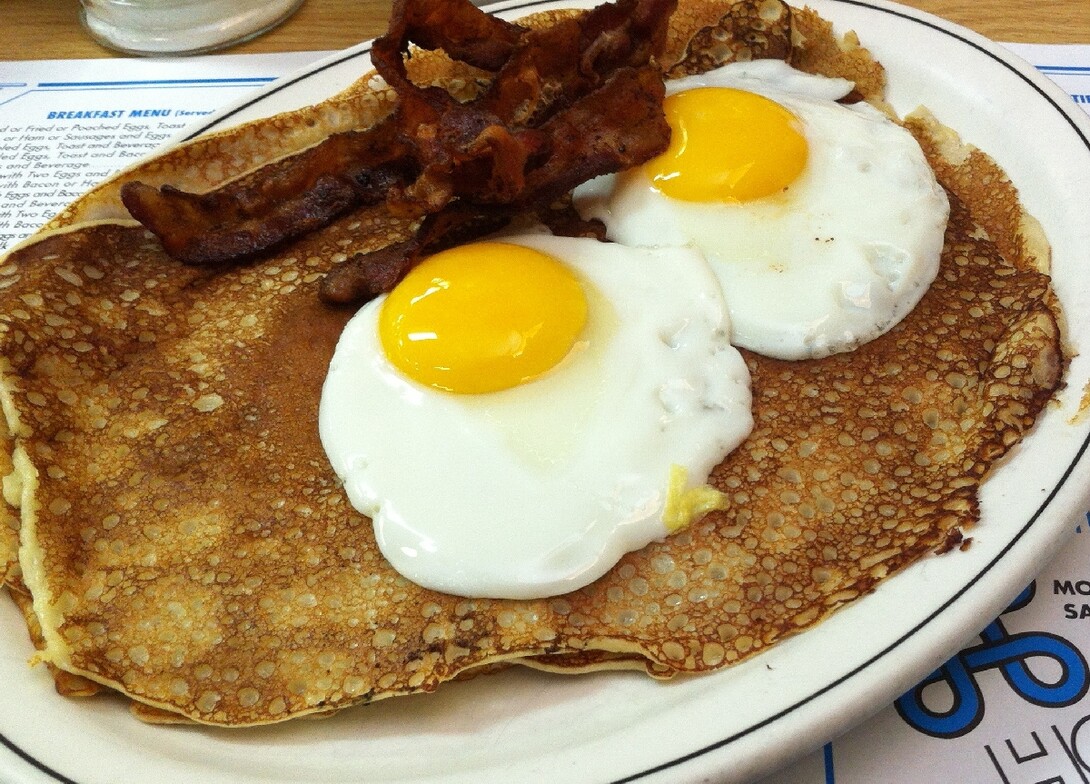 Finnish pancakes topped with two eggs and bacon sitting on top of a Hoito's menu.