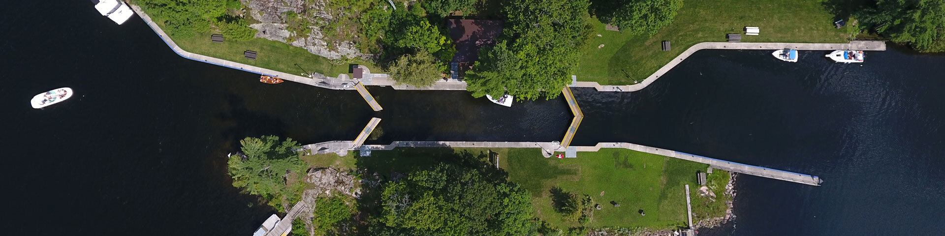 Locks on the Trent-Severn Waterway from above; a dark water channel segemented by open locks and surrounded by green grass and forest.