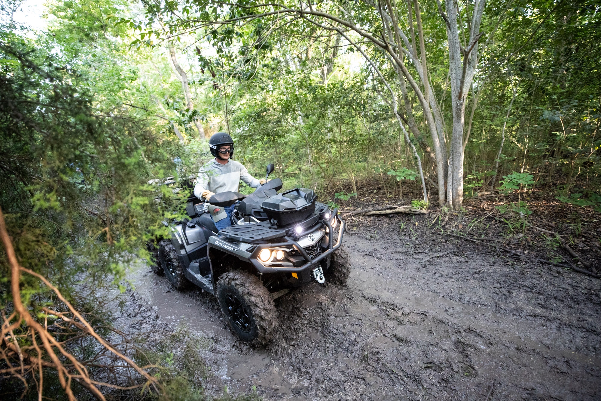 An ATV rider on a muddy road in a forest.