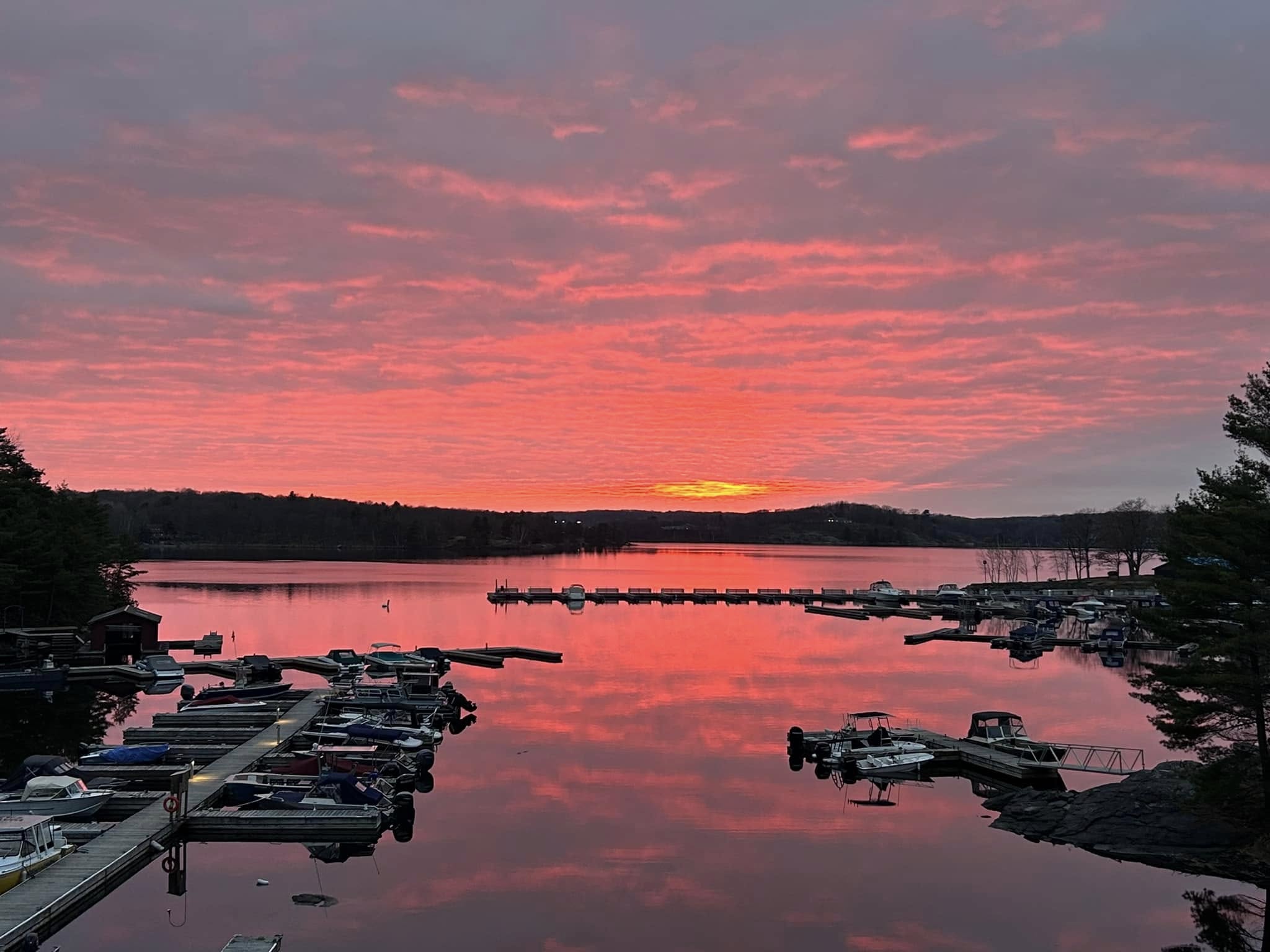 Georgian Bay Marina, with small boats docked on calm glassy water, lit up by a vibrant orange sunset. 