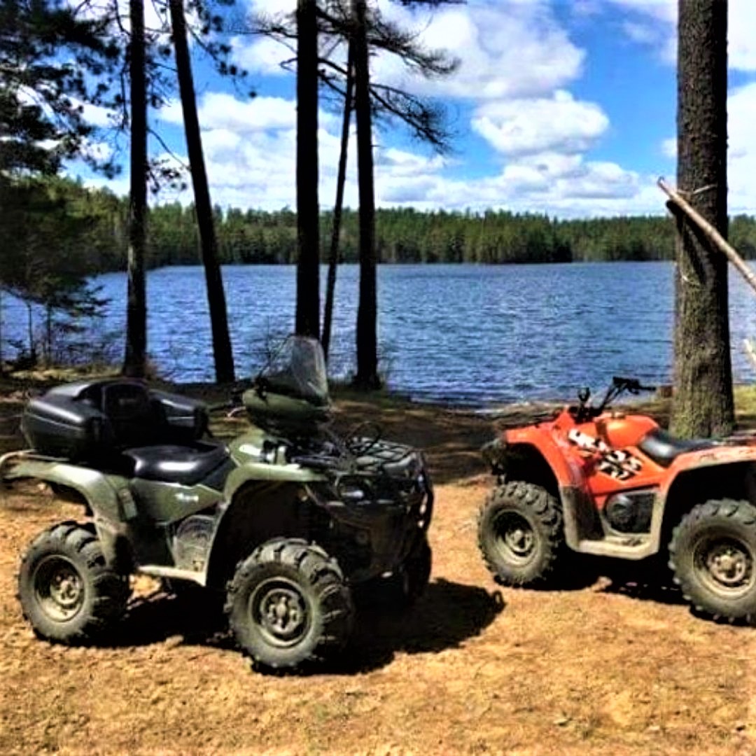 Two ATVs parked in front of a lake. 