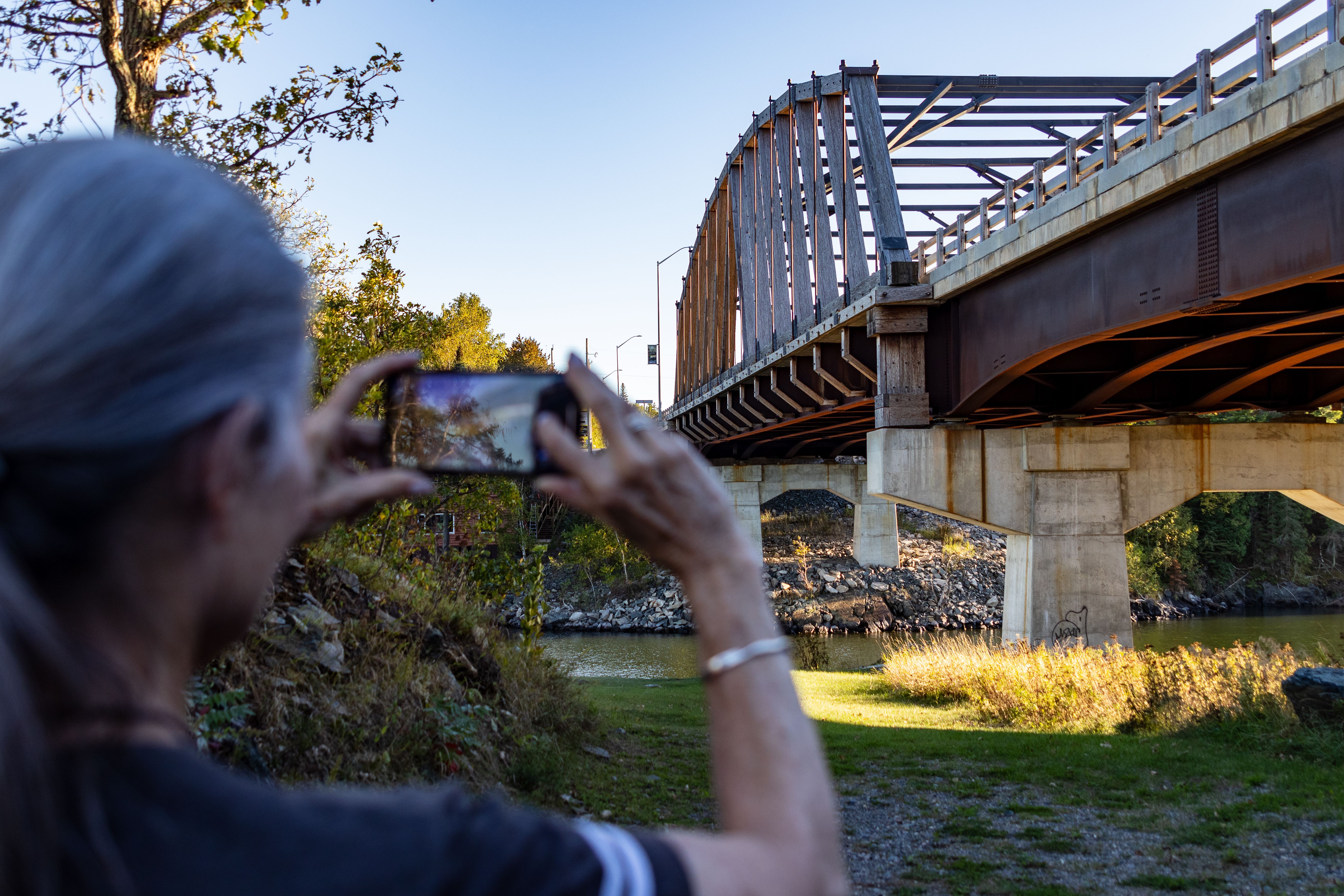 A woman takes a photo of the large wooden heritage bridge at Sioux Narrows on a summer day.