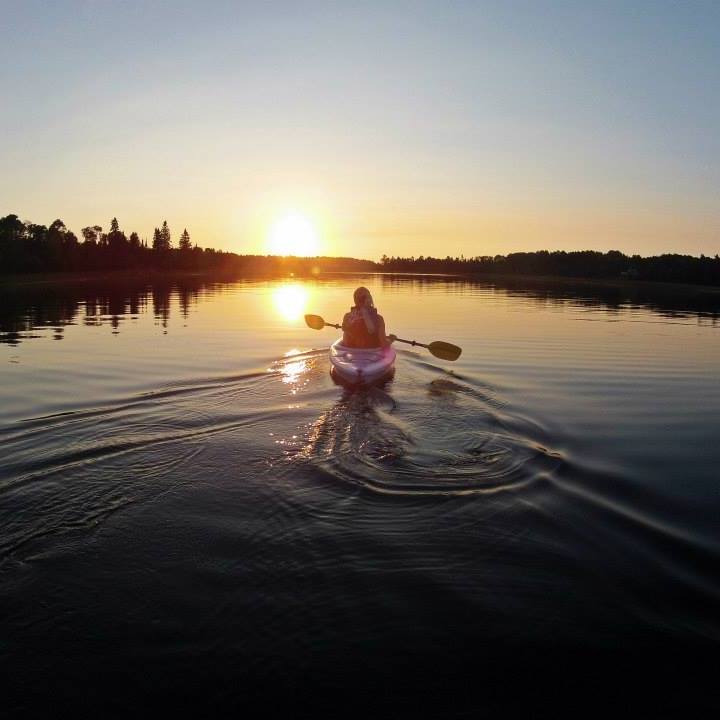 A person paddles a kayak along glassing water at sunset in Sioux Narrows.