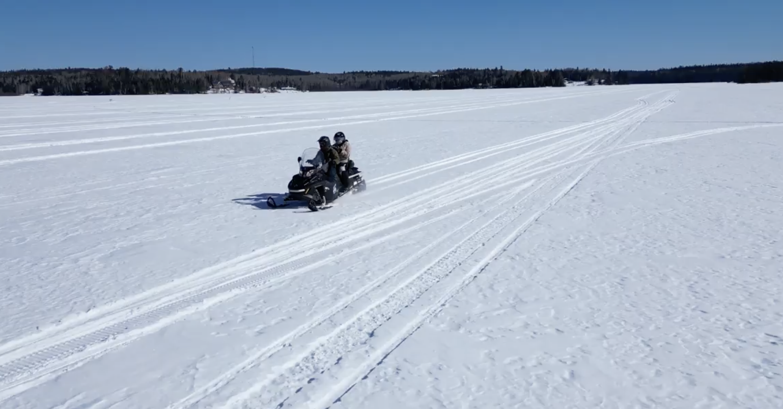 Two people ride a snowmobile across a frozen lake on a sunny winter day.