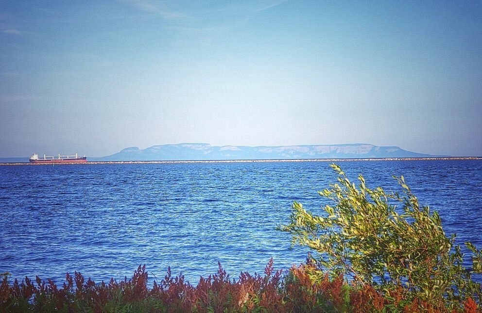 The misty silhouette of Sleeping Giant on the horizon across the bright blue waters of Lake Superior. 