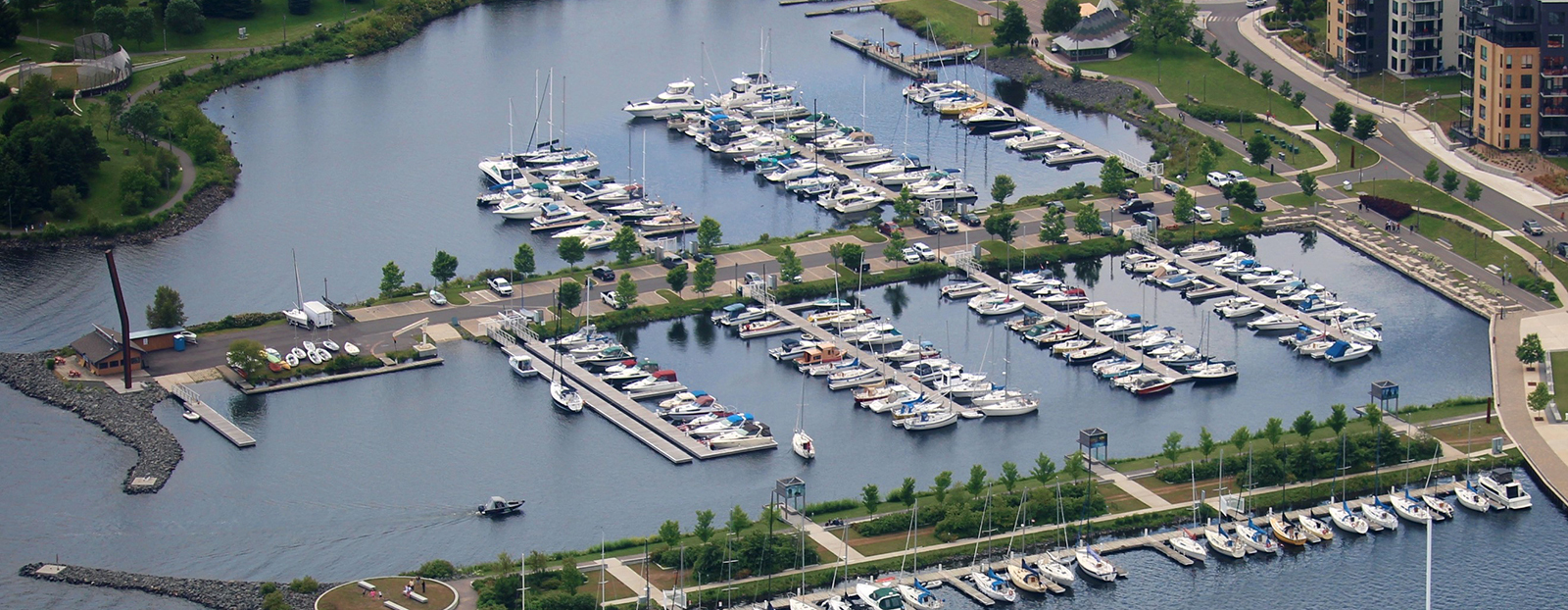 Thunder Bay Marina; a busy marina surrounded by green trees and cityscape on the shore of Lake Superior.