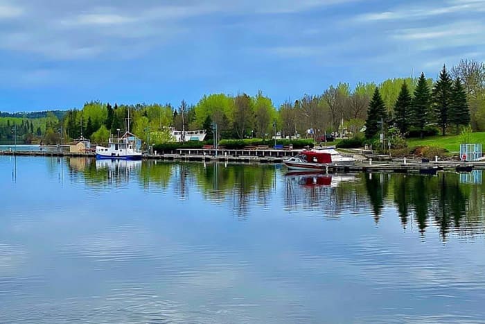 The Nipigon Marina; glassy water reflecting a blue sky and green forested shoreline dotted with boats.